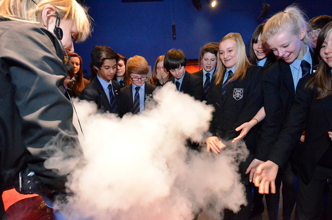 School children observing a science experiment which is producing smoke.