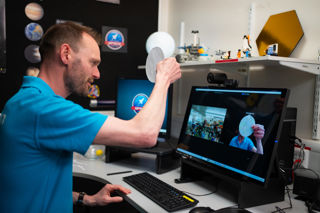 An Education Presenter conducting a Video Conference with a School Group, holding up a circular piece of paper with an image of the Earth on it.
