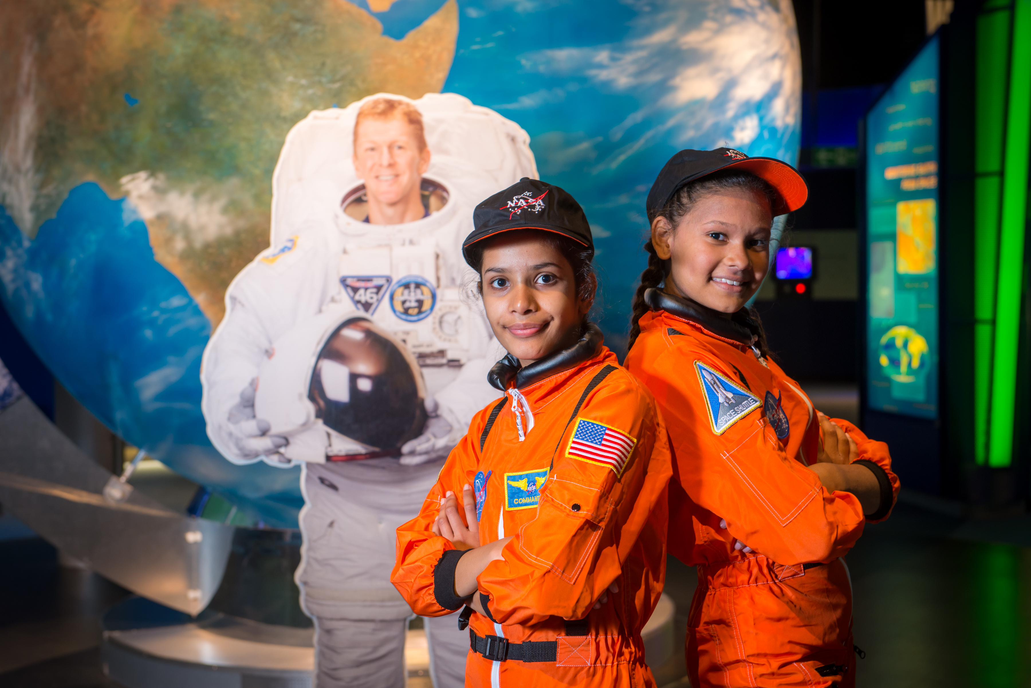 Two girls in orange spacesuits with Tim Peake